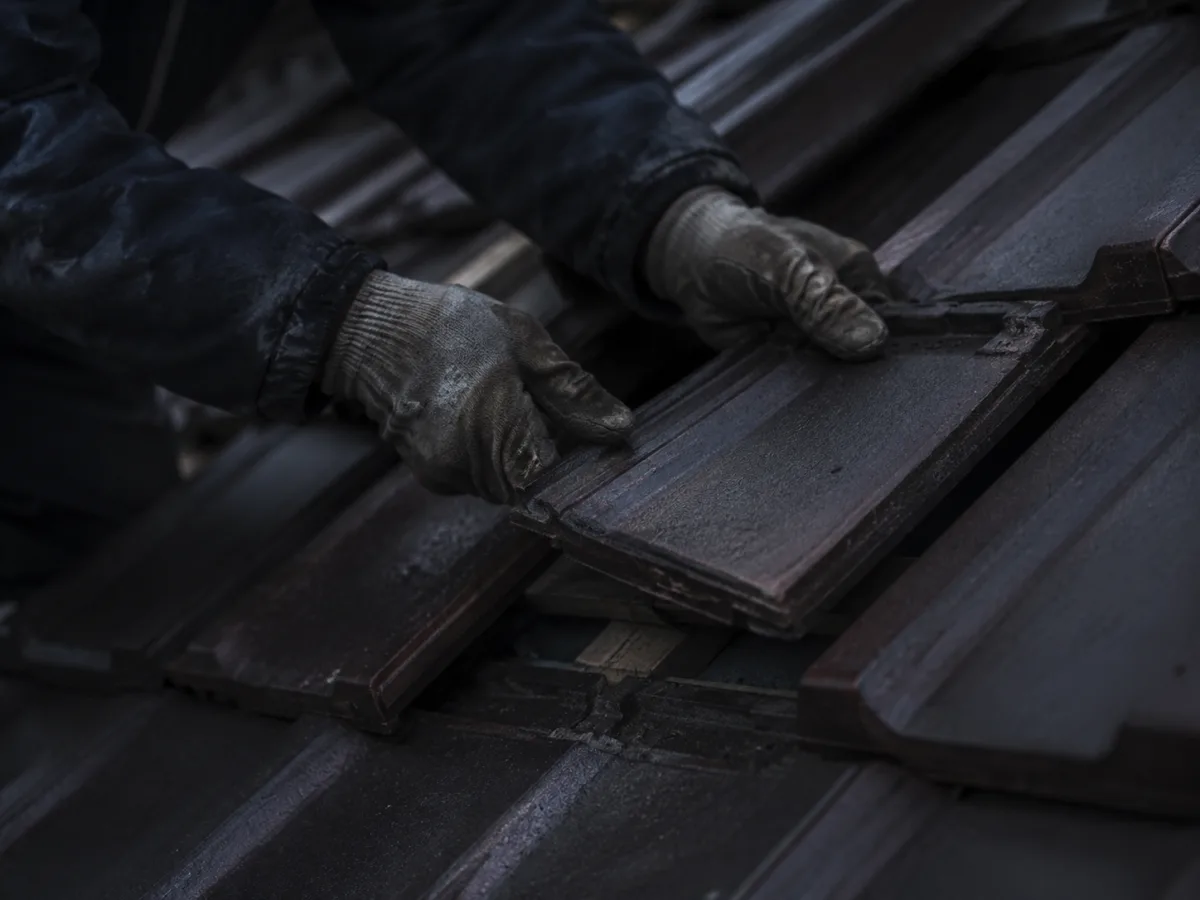 Hände in Arbeitshandschuhen legen einen Dachziegel